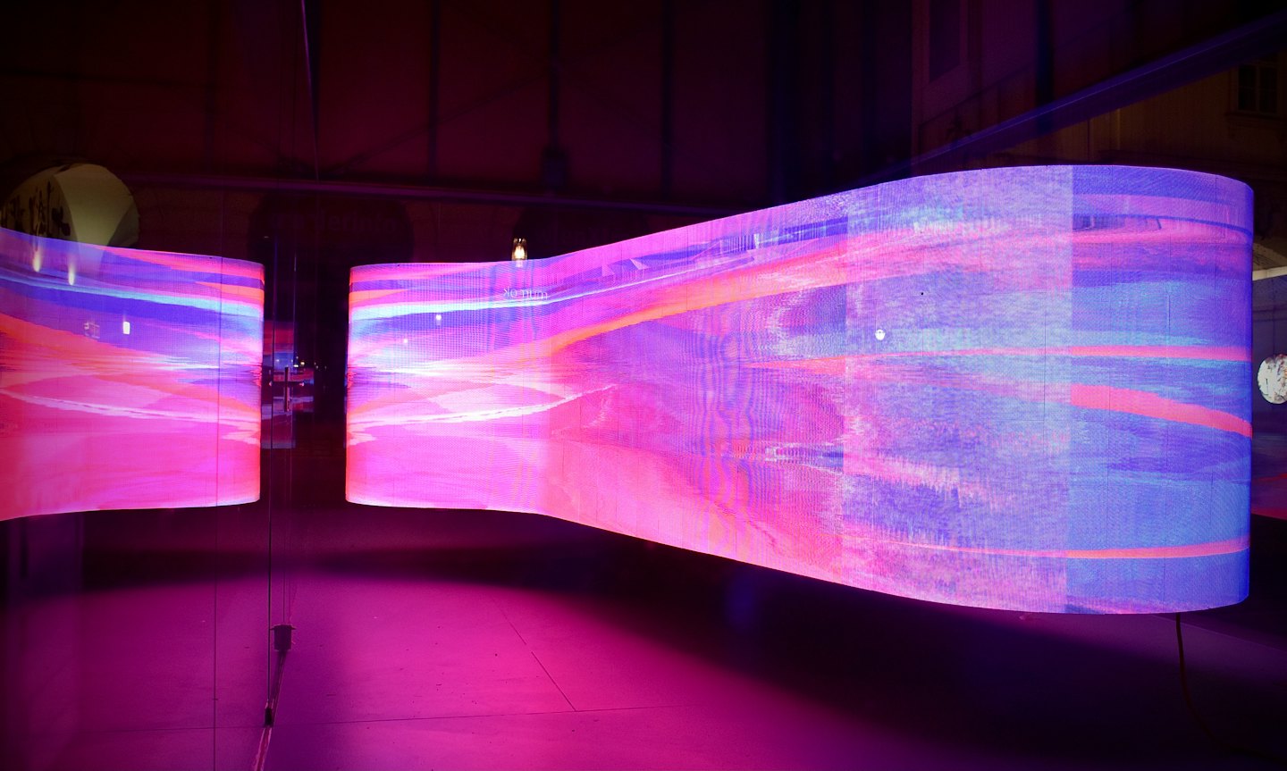 Curved LED screens show vibrant abstract art in a dark room.