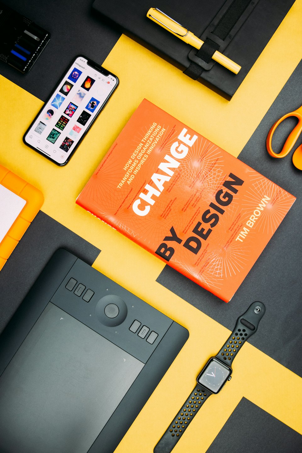 Creative tools including a tablet, phone, and book on a black and yellow background.